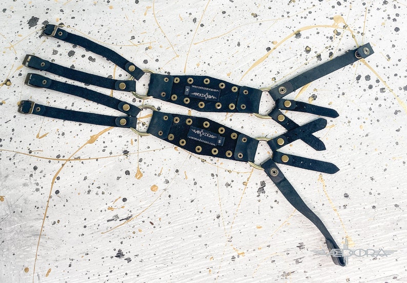 May include: Two black leather straps with gold metal rings and buckles. Each strap has a black leather patch with the word "Volition" printed in white.