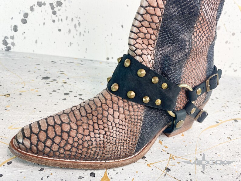 May include: A pair of brown and black snakeskin boots with a black leather strap with gold studs and a metal ring.