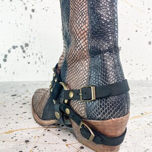 May include: Black and brown snakeskin ankle boots with a gold buckle and studded strap. The boots have a stacked heel and a pointed toe.