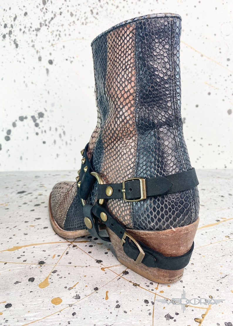 May include: Black and brown snakeskin ankle boots with a gold buckle and studded strap. The boots have a stacked heel and a pointed toe.