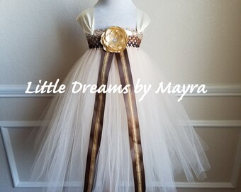 May include: A white tulle dress with brown and gold ribbon accents. The dress has a satin bodice with a gold flower embellishment. The dress is on a wooden mannequin.