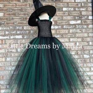 May include: A black and dark green witch costume featuring a pointed black hat and a dress with a black crocheted bodice and a full, layered tulle skirt in alternating black and dark green colors. The text Little Dreams by Mayla is visible.