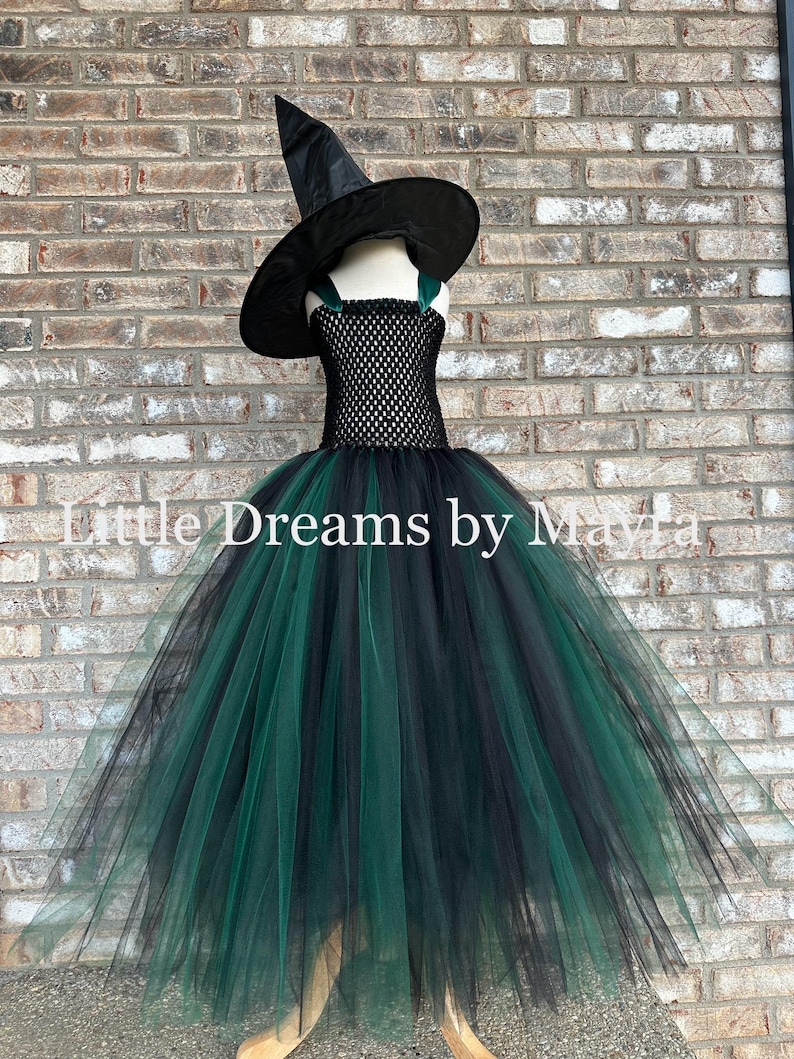 May include: A black and dark green witch costume featuring a pointed black hat and a dress with a black crocheted bodice and a full, layered tulle skirt in alternating black and dark green colors. The text Little Dreams by Mayla is visible.