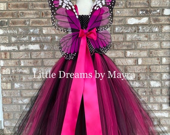 Könnte beinhalten: Ein schwarzer und magentafarbener Tüll-Tutu mit einem rosa Satinband und Schmetterlingsflügeln. Die Flügel sind schwarz, magenta und weiß mit schwarzen Punkten. Der Tutu ist geschichtet und hat ein schwarzes Oberteil.