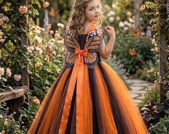 Könnte beinhalten: Ein bodenlanges Kleid mit einem schwarzen Oberteil mit weißen Punkten und einem voluminösen Rock aus abwechselnden Lagen von orangefarbenem und schwarzem Tüll. Der Rücken des Kleides ist mit Monarchfalterflügeln und einer orangefarbenen Satinschleife verziert.
