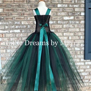 May include: A sleeveless dress featuring a black crocheted bodice and a voluminous skirt made of layered black and dark green tulle. The dress includes dark green satin shoulder straps and a matching satin ribbon tied in a bow at the waist.