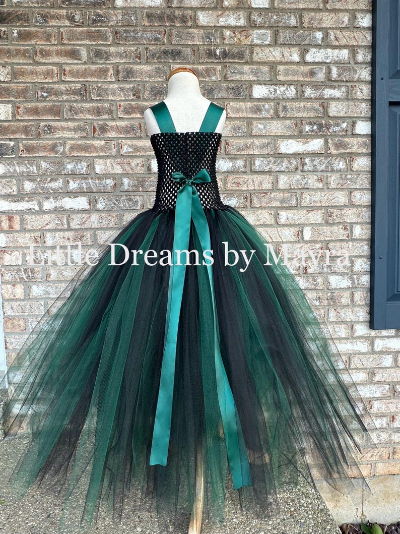 May include: A sleeveless dress featuring a black crocheted bodice and a voluminous skirt made of layered black and dark green tulle. The dress includes dark green satin shoulder straps and a matching satin ribbon tied in a bow at the waist.