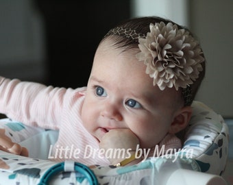 May include: A baby wearing a pink and white striped shirt with a brown flower headband. The baby is sitting in a high chair and has a hand in their mouth.
