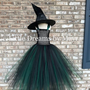 May include: A black and dark green witch costume featuring a pointed hat and a dress with a crocheted bodice and a layered tulle skirt. The text Little Dreams by Mayra is visible across the center of the image over the brick wall background.