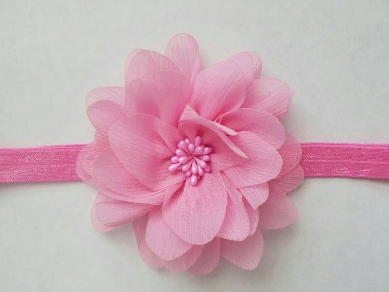 K&ouml;nnte beinhalten: Ein rosa Stoffblumen-Haarreif mit einem Zentrum aus rosa perlenartigen Perlen.