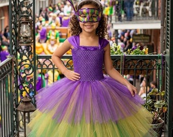 May include: A floor-length dress featuring a purple crocheted bodice with thick straps and a multi-layered tulle skirt in shades of purple, yellow, and green. The outfit is paired with a decorative silver crown and a purple, green, and gold eye mask.