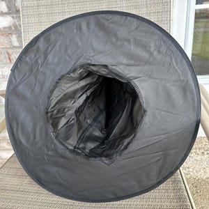 May include: A black pointed hat with a wide, circular brim and a tall, conical crown. The hat is constructed from a smooth, lightweight fabric with visible stitching along the inner rim where the crown meets the brim, creating a hollow interior.