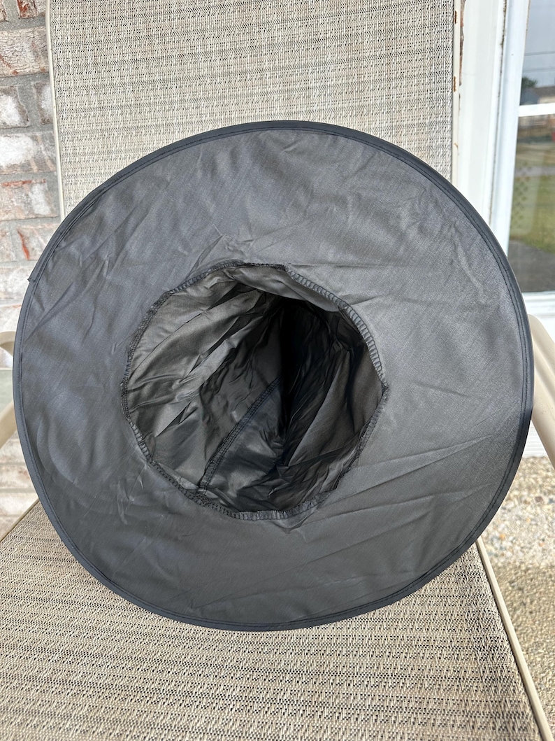 May include: A black pointed hat with a wide, circular brim and a tall, conical crown. The hat is constructed from a smooth, lightweight fabric with visible stitching along the inner rim where the crown meets the brim, creating a hollow interior.