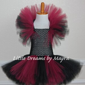 May include: A black and burgundy tulle tutu with a black mesh bodice. The tutu has a ruffled top layer and a black tulle bottom layer. The bodice has a black mesh design. The tutu is on a white background. "Little Dreams by Mayra" is written on the tutu.
