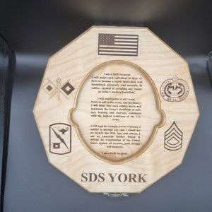 Puede incluir: Una placa octogonal de madera con una cita sobre ser sargento de instrucci&oacute;n en el ej&eacute;rcito de los Estados Unidos. La placa presenta la bandera estadounidense, un insignia militar y el texto "SDS YORK".
