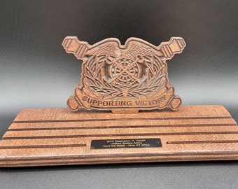 以下が含まれることがあります： 「Supporting Victory」という文字が刻まれた木製の銘板。その下に「SPC Rasheem R. Rasiff, United States Army, Apr 03 2003 - May 01 2022」と刻まれた小さな銘板がある。