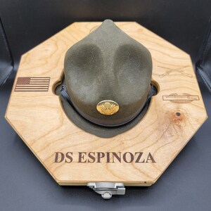May include: A wooden octagonal hat display with a green military hat, a US flag, crossed rifles, and the text "DS ESPINOZA".