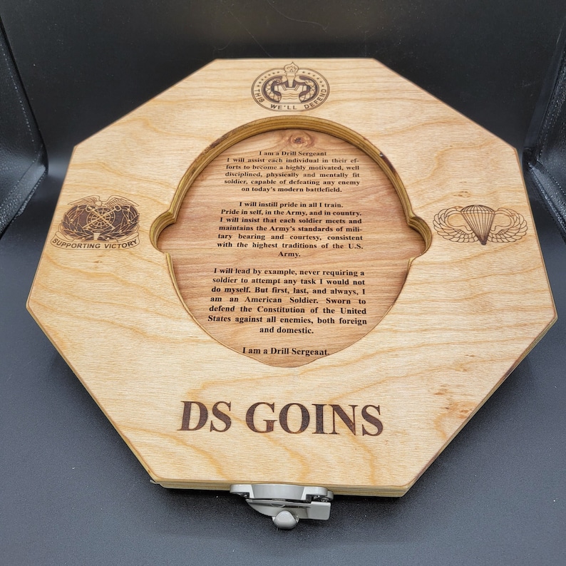 May include: A wooden plaque with a cutout for a military patch. The plaque features a quote about the duties of a Drill Sergeant, followed by the text "DS GOINS".
