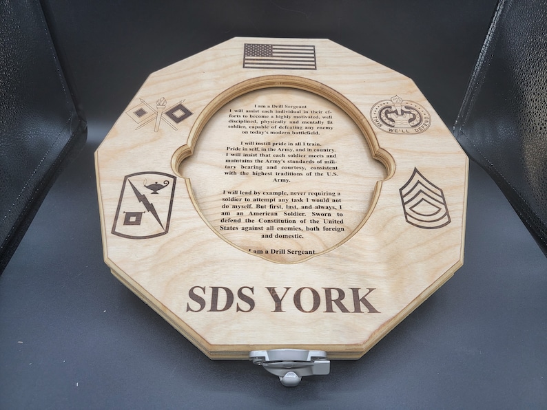 Puede incluir: Una placa de madera con una cita sobre los deberes de un sargento de instrucci&oacute;n en el ej&eacute;rcito de los Estados Unidos. La placa es octogonal y presenta una variedad de insignias militares, incluido el logotipo del ej&eacute;rcito de los Estados Unidos, un rayo y una l&aacute;mpara, y un gal&oacute;n. El texto dice: "Soy un sargento de instrucci&oacute;n... Dar&eacute; el ejemplo, nunca pidiendo a un soldado que intente una tarea que yo no har&iacute;a. Pero primero, &uacute;ltimo y siempre, soy un soldado estadounidense. Jurado para defender la Constituci&oacute;n de los Estados Unidos contra todos los enemigos, tanto extranjeros como nacionales. Soy un sargento de instrucci&oacute;n." La placa est&aacute; firmada "SDS YORK".