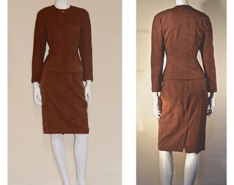 May include: A brown skirt suit with a fitted jacket and a straight skirt. The fabric has a subtle embossed pattern.