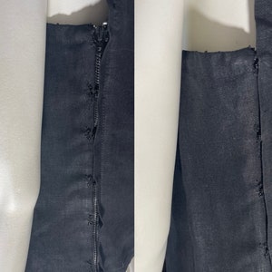 May include: Close-up of a black garment with a zipper and stitching details. The fabric appears to be a dark, solid color, possibly linen or a similar material. The zipper is visible along the seam.