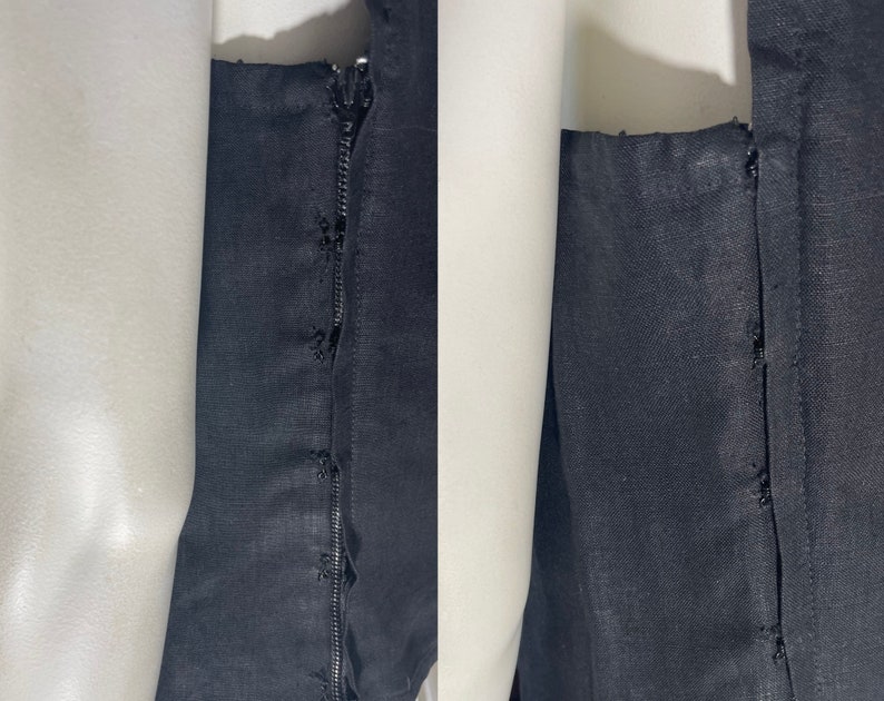 May include: Close-up of a black garment with a zipper and stitching details. The fabric appears to be a dark, solid color, possibly linen or a similar material. The zipper is visible along the seam.