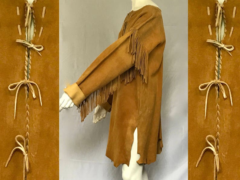 May include: A tan suede tunic with long sleeves and fringe detail on the sleeves. The tunic has a split on the side and is displayed on a mannequin. The side panels feature decorative stitching.