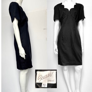 May include: A black dress with a scalloped neckline and short sleeves. The dress is made by the brand "Scasso" and has a label that says "Dress".