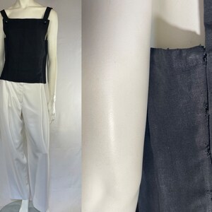 May include: A black tank top with square straps and button details, paired with white pleated trousers. The top is sleeveless and the trousers have a high waist. The outfit is displayed on a mannequin.