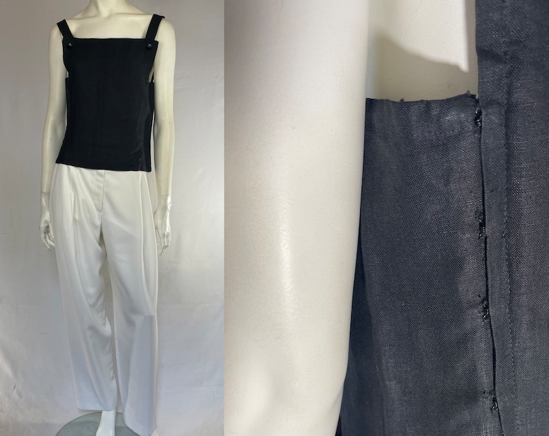 May include: A black tank top with square straps and button details, paired with white pleated trousers. The top is sleeveless and the trousers have a high waist. The outfit is displayed on a mannequin.