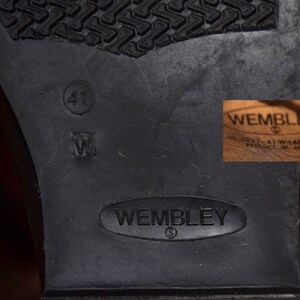 May include: Close-up of the sole of a black leather shoe with the brand name "Wembley" embossed on the bottom. The shoe size is marked as "41" and "W" on the sole. The shoe is made in Japan.