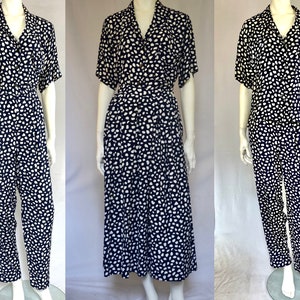 May include: A navy blue and white patterned jumpsuit with short sleeves and a collared neckline. The jumpsuit has a wrap-style waist and a relaxed fit.