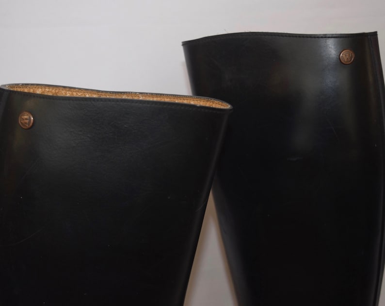 May include: A pair of black leather riding boots with a brown leather trim around the top of the boot. The boots have a small metal buckle on the side.