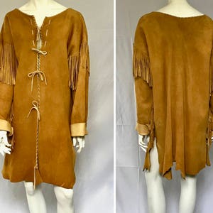 May include: A tan suede coat with long sleeves, fringe detailing on the sleeves, and a braided tie closure down the front. The coat has a V-neckline and tan cuffs. The coat is knee-length.