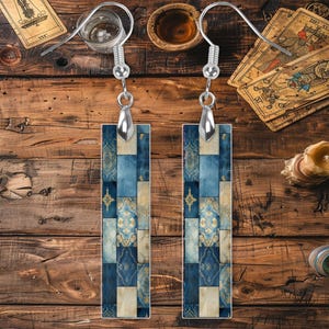 May include: A pair of silver earrings with blue and cream rectangular tile-patterned charms. The charms have a geometric design with a floral motif.