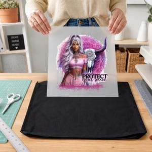 May include: A square heat transfer sheet featuring a graphic of a person with long light hair, a pink top, and tattoos, positioned next to a stylized bull skull and a purple mandala. The text "PROTECT your peace" is printed in black and purple.