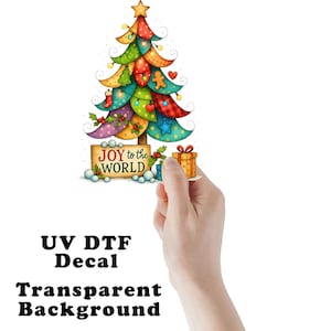 May include: A colorful Christmas tree decal featuring layered, patterned branches in red, green, blue, and yellow. The tree is topped with a gold star and decorated with ornaments. A wooden sign at the base reads JOY to the WORLD with a gift box.