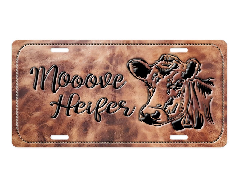 May include: A brown leather license plate with a black stitched border. The plate features a black silhouette of a cow's head and the text "Mooove Heifer".