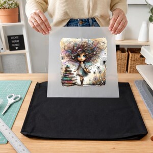 May include: A square, semi-transparent transfer sheet featuring a whimsical illustration of a wide-eyed character with voluminous, swirling hair standing beside a tall stack of colorful books and dandelion flowers, held above a plain black fabric tote bag.