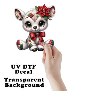 May include: A UV DTF decal featuring a cartoon deer with large eyes, wearing a red bow and a poinsettia flower on its head. The deer has a white body with patches of red, green, and white quilted patterns. The text reads UV DTF Decal Transparent Background.