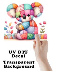 May include: A colorful koala bear decal with a patchwork design. The koala is holding a small pink flower and is surrounded by decorative plants. The text "UV DTF Decal Transparent Background" is printed at the bottom.