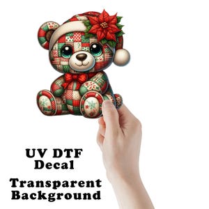 May include: A UV DTF decal featuring a teddy bear with a patchwork pattern in red, green, and white. The bear wears a matching patchwork Santa hat adorned with a red poinsettia flower. The text UV DTF Decal Transparent Background is visible.