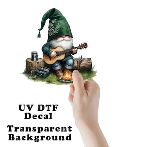 May include: A green gnome with a white beard is sitting on a log playing a brown acoustic guitar. The gnome is wearing a green hat with a leaf design. The gnome is sitting by a small campfire.  UV DTF Decal Transparent Background