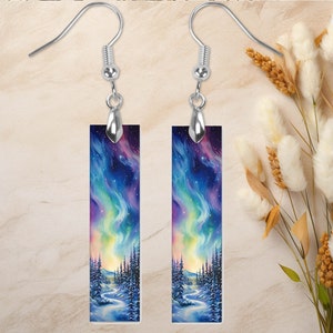 May include: A pair of silver dangle earrings with rectangular glass panels featuring a watercolor painting of a snowy forest scene with a vibrant aurora borealis in the sky.