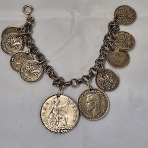 May include: A charm bracelet featuring a series of bronze-toned Canadian one-cent coins dated 1951, a 1936 British one-penny coin, and a coin depicting King George VI, all attached to a circular link chain with a small round clasp at one end.