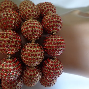 May include: A bracelet made of large, round, red beads covered in sparkling rhinestones. The beads are arranged in a layered design, creating a bold and eye-catching look.
