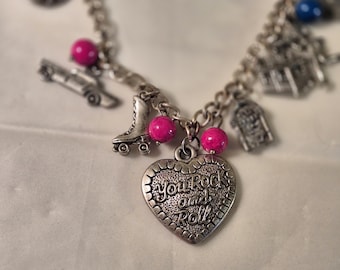 May include: Silver charm bracelet with various charms, including a roller skate, car, and a heart-shaped pendant. The heart pendant has the words "You Rock and Roll" engraved on it. The bracelet also features pink beads.