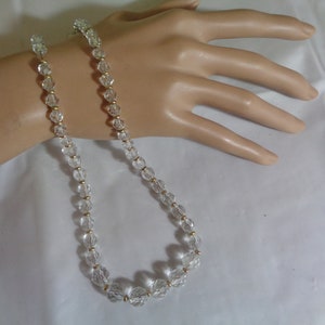 May include: A clear crystal beaded necklace with gold accents. The necklace is strung on a thin gold chain.