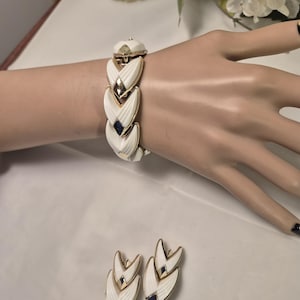May include: A vintage jewellery set comprising a bracelet and matching earrings. The bracelet and earrings feature a white enamel finish with gold-tone accents and a geometric design. The earrings and bracelet have a dark blue accent.