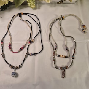 May include: Two layered necklaces with beaded accents. One necklace has a blue and white pendant, the other has a copper-coloured leaf pendant. Both necklaces have a variety of colourful beads.